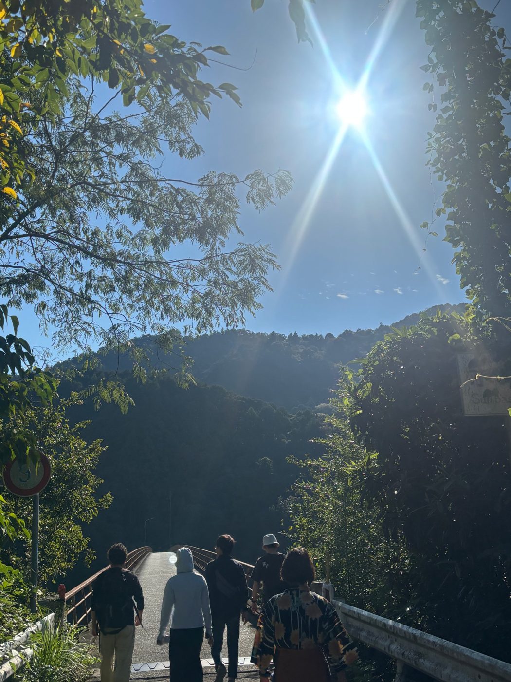 晴れた空の下、山へ続く橋を歩く人たち